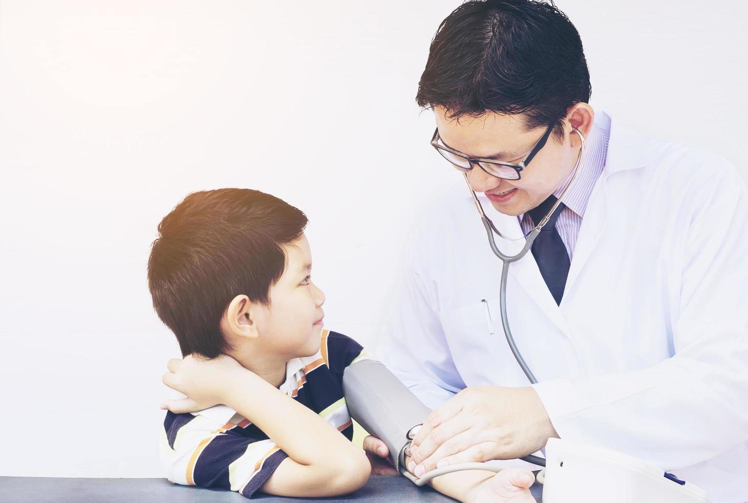 Asian boy being examined by male doctor using stethoscope and blood pressure monitor over white background photo