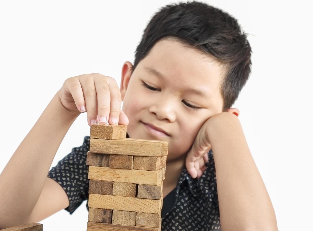 un niño asiático está jugando jenga, un juego de torre de bloques de madera para practicar habilidades físicas y mentales foto