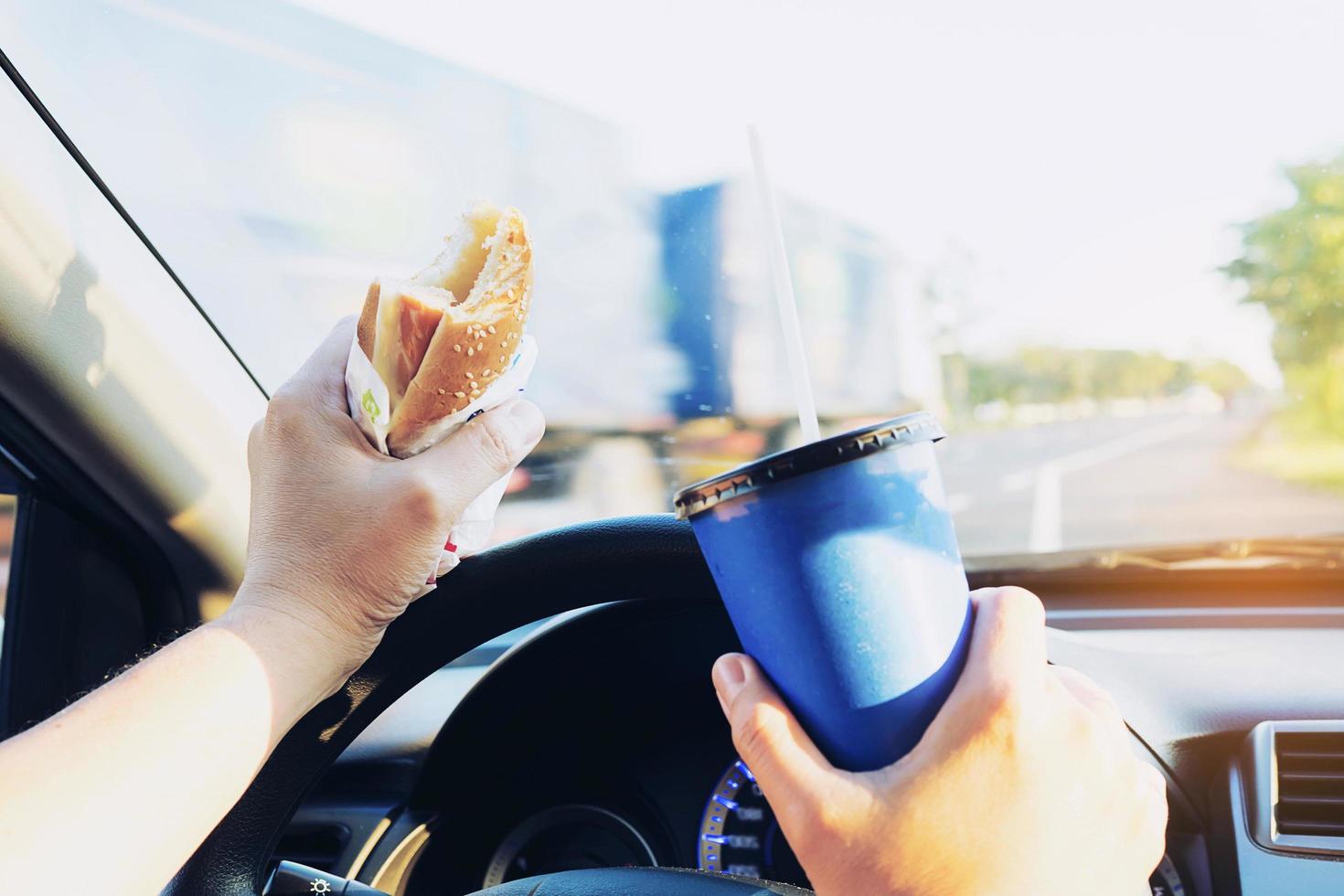 Man is dangerously eating hot dog and cold drink while driving a car photo