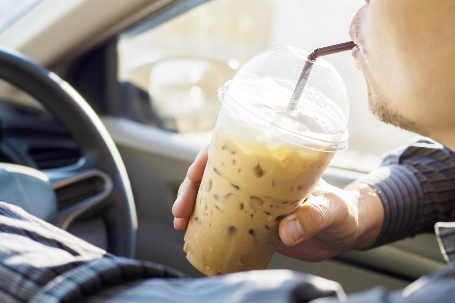 Man is dangerously drinking cup of cold coffee while driving a car photo