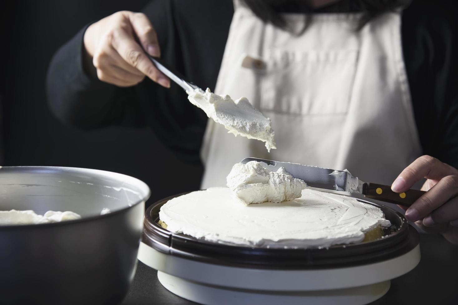 señora haciendo pastel poniendo crema con espátula - concepto de cocina de panadería casera foto