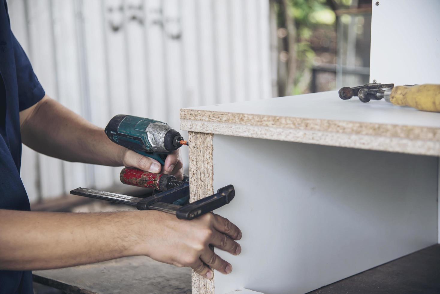 el hombre está trabajando con el montaje de muebles usando un destornillador eléctrico - trabajo técnico en el sitio usando el concepto de herramientas manuales foto