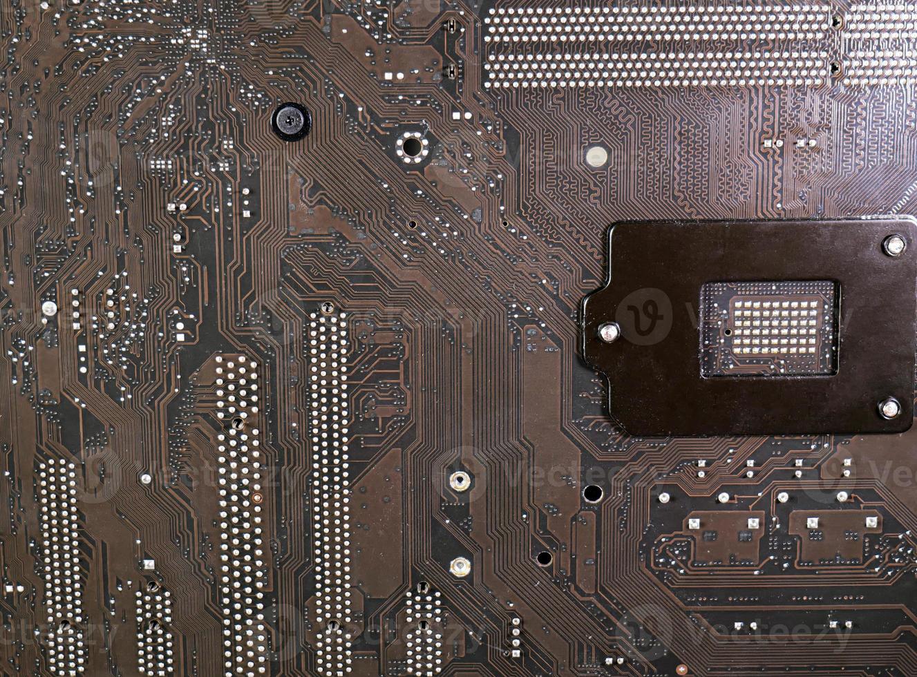 The surface of the motherboard, dark brown, has a pattern of data paths, and the current has a point caused by lead solder. It's the circuit board under the CPU. photo