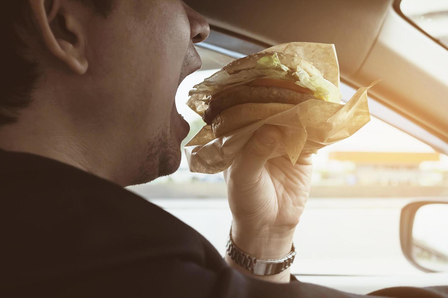 Man driving car while eating hamburger photo