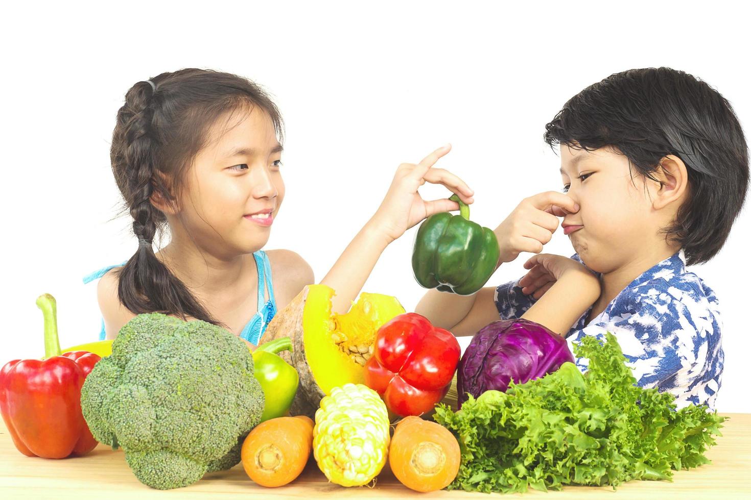 Asian boy and girl showing dislike expression  with fresh colorful vegetables isolated over white background photo