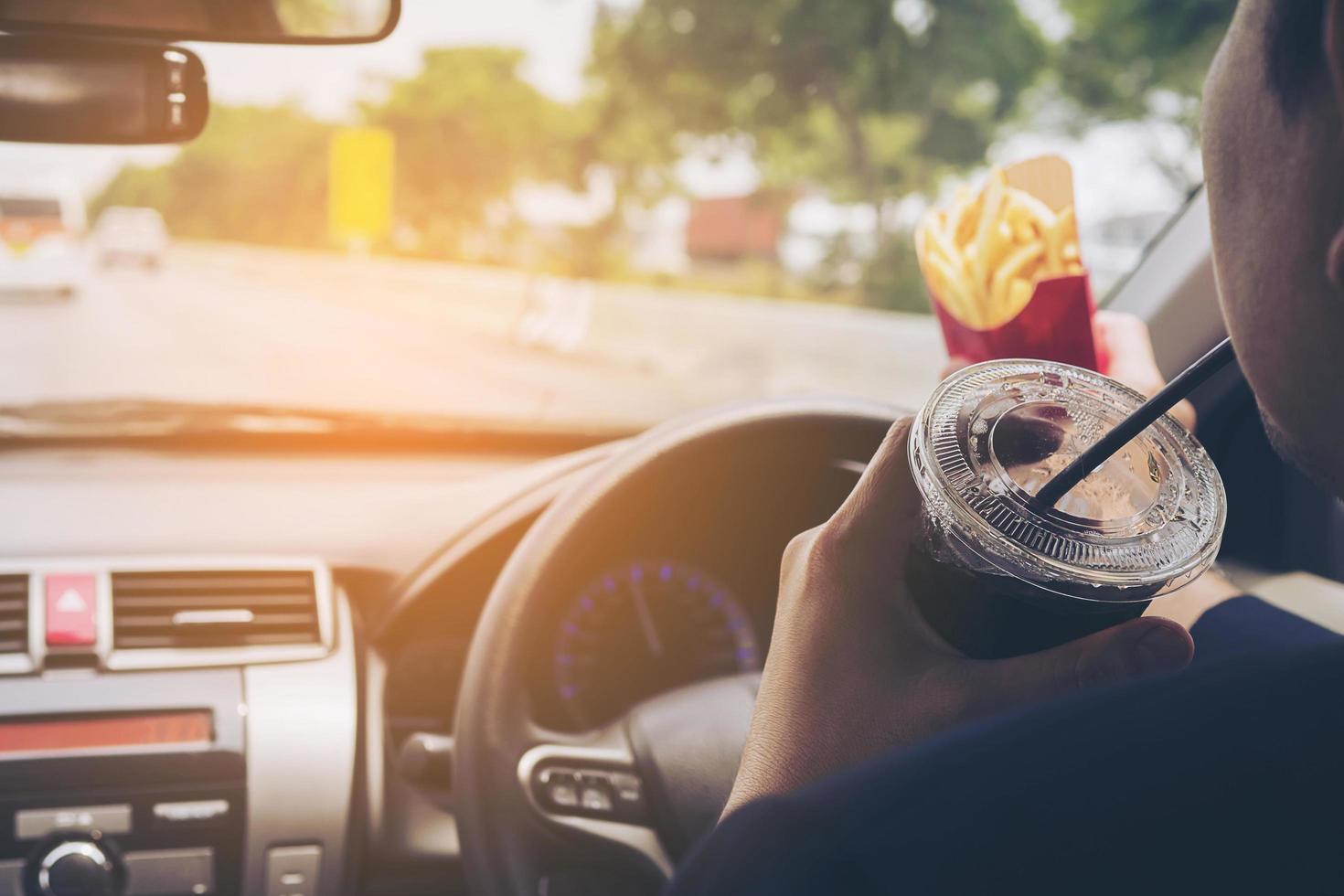 Man driving car while eating French fries and soft drink, left-driving countries photo