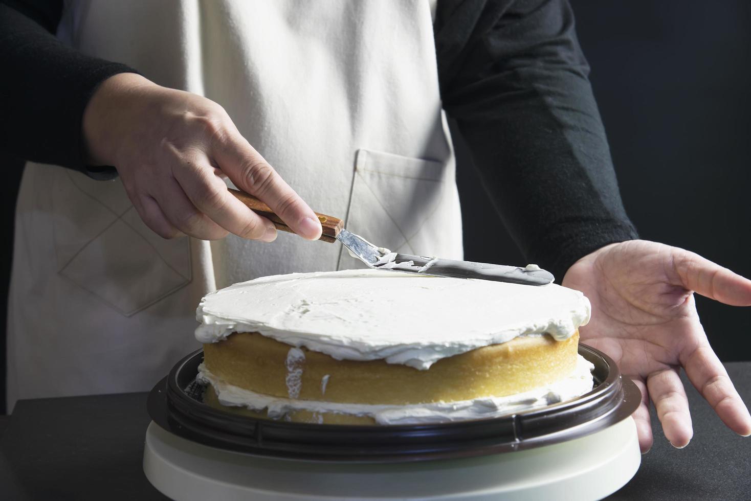 señora haciendo pastel poniendo crema con espátula - concepto de cocina de panadería casera foto