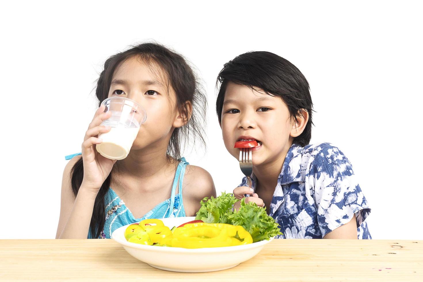 Asian boy and girl showing enjoy expression with fresh colorful vegetables and glass of milk isolated over white background photo