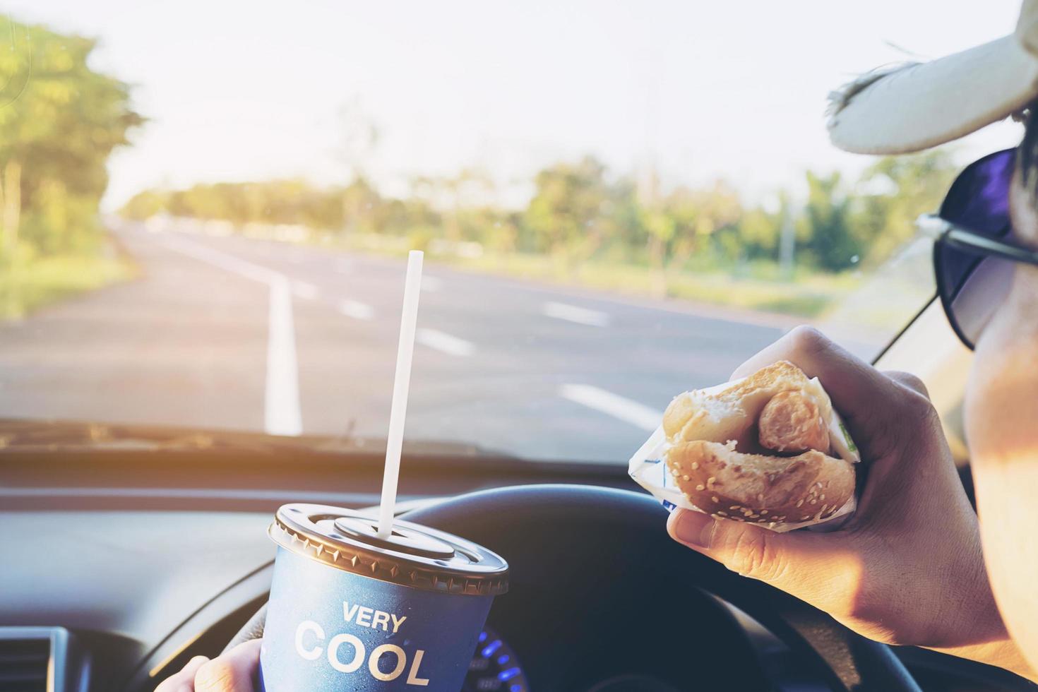 Man is dangerously eating hot dog and cold drink while driving a car photo