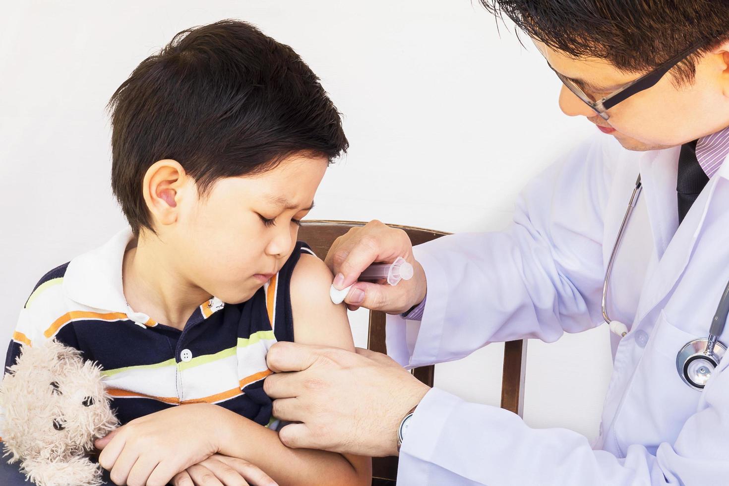 Sick Asian boy being treated by male doctor over white background photo