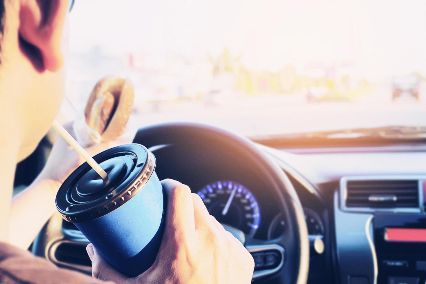 Man is dangerously eating hot dog and cold drink while driving a car photo