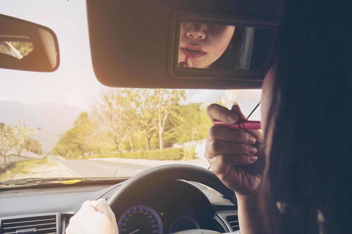 Woman making up her face using lipstick while driving car, unsafe behavior photo