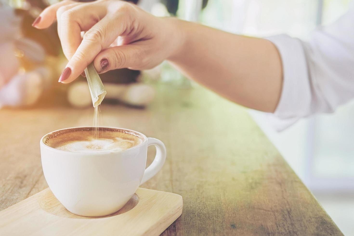 Closeup of lady pouring sugar while preparing hot coffee cup photo