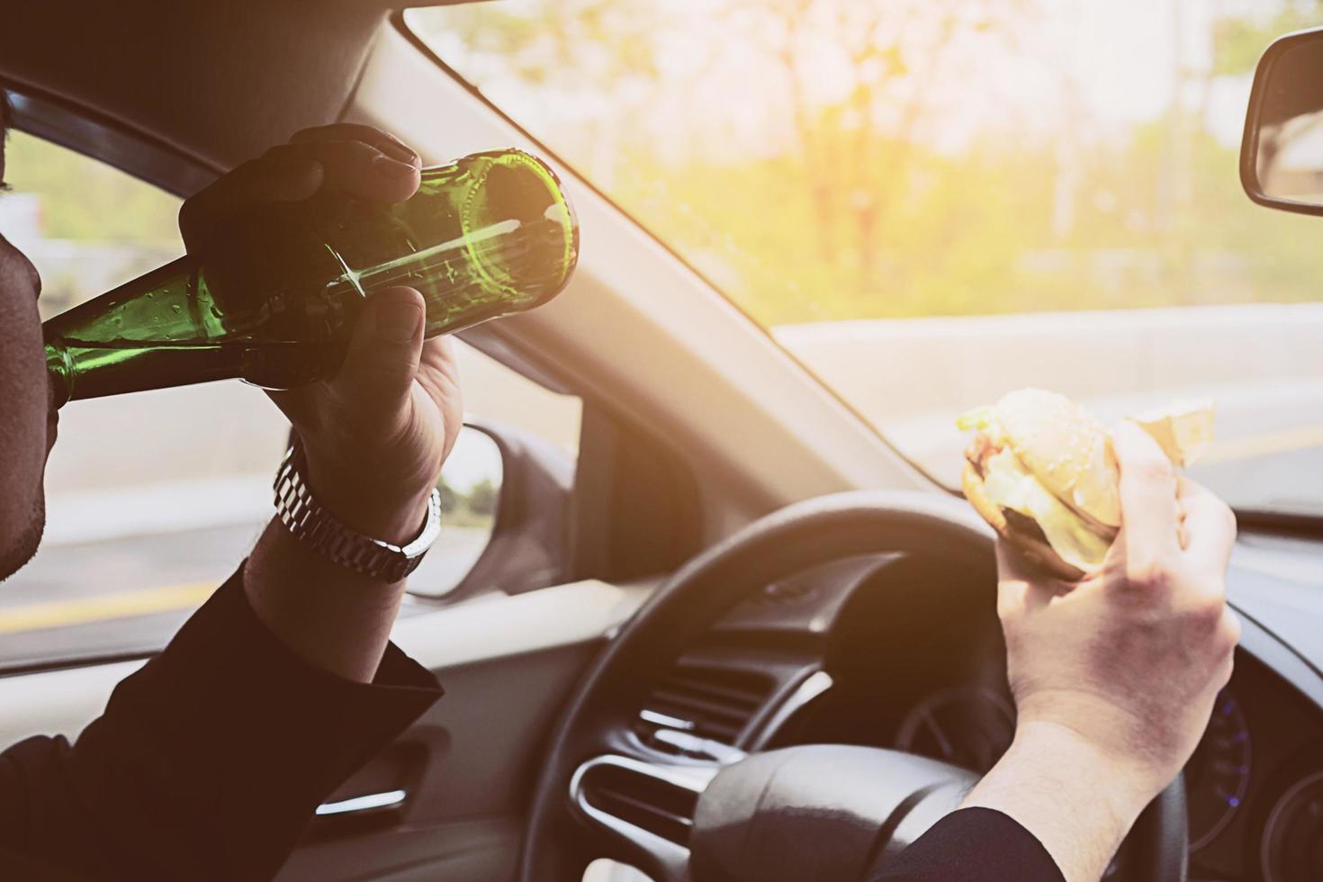 hombre conduciendo un coche mientras come hamburguesas y bebe cerveza foto