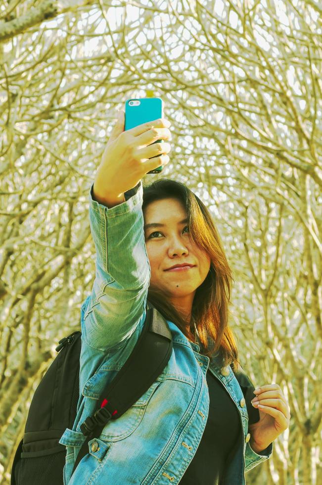 Young asian lady taking selfie photo using mobile phone with pumaria tree background