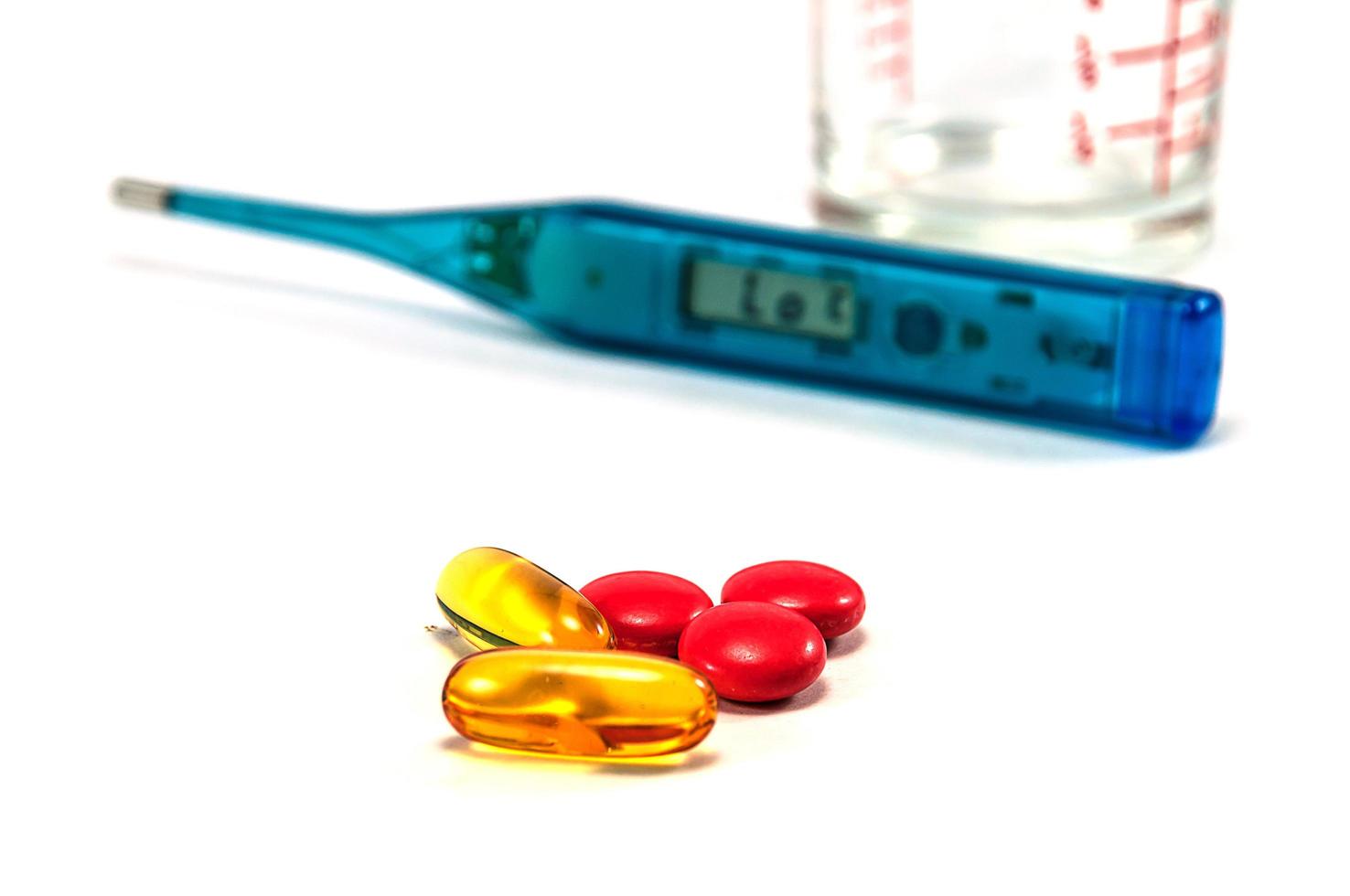 Fish oil and medicine pills with blurred thermometer and glass on white background photo