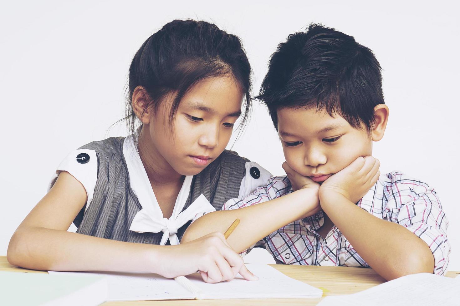 Sister try to teach her naughty younger brother to do homework  isolated over white background photo