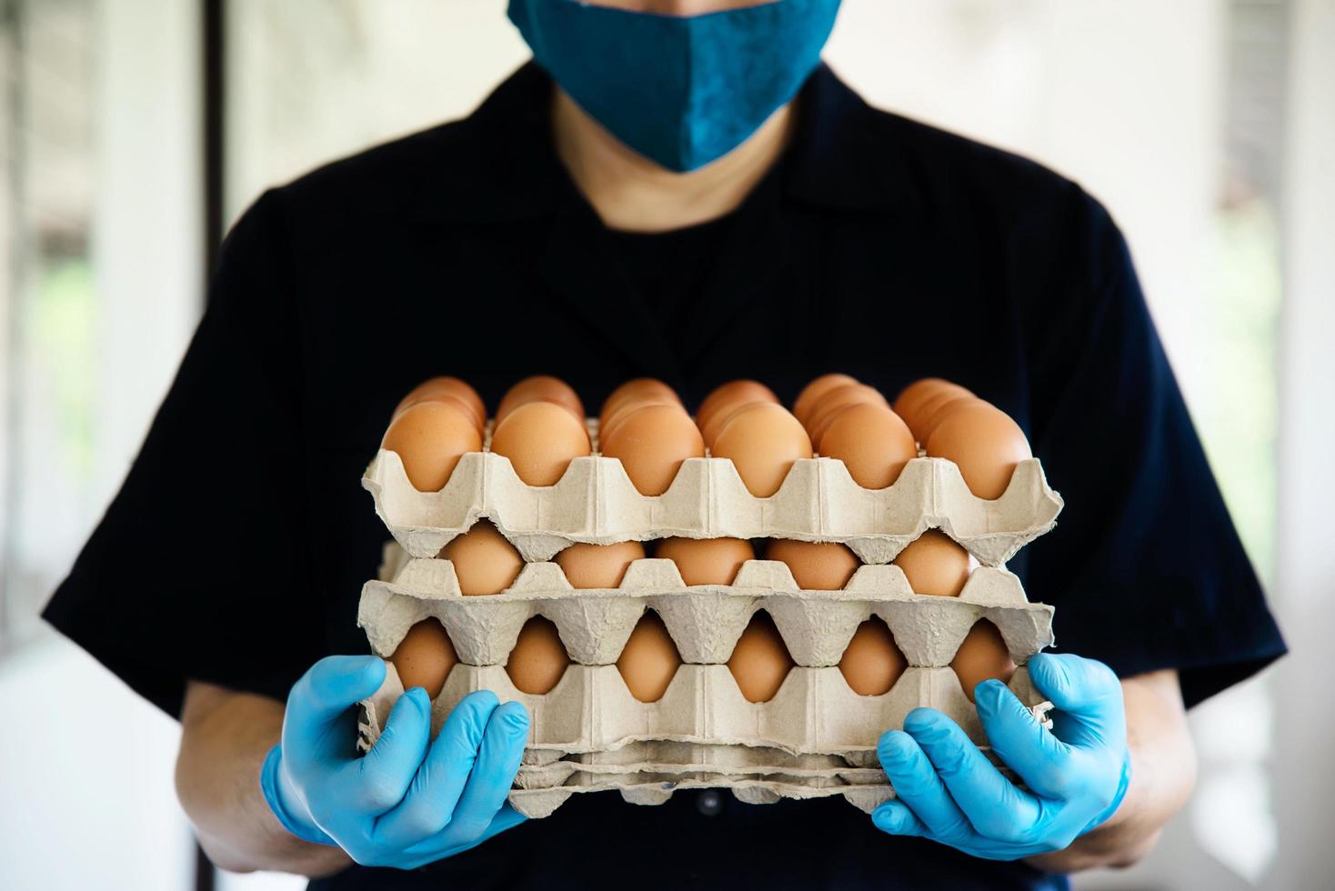 A man carry 3 layers eggs tray for stay safe at home putting sanitary glove during corona virus COVID-19 spreading - people keeping food in COVID-19 viral spread period concept. photo