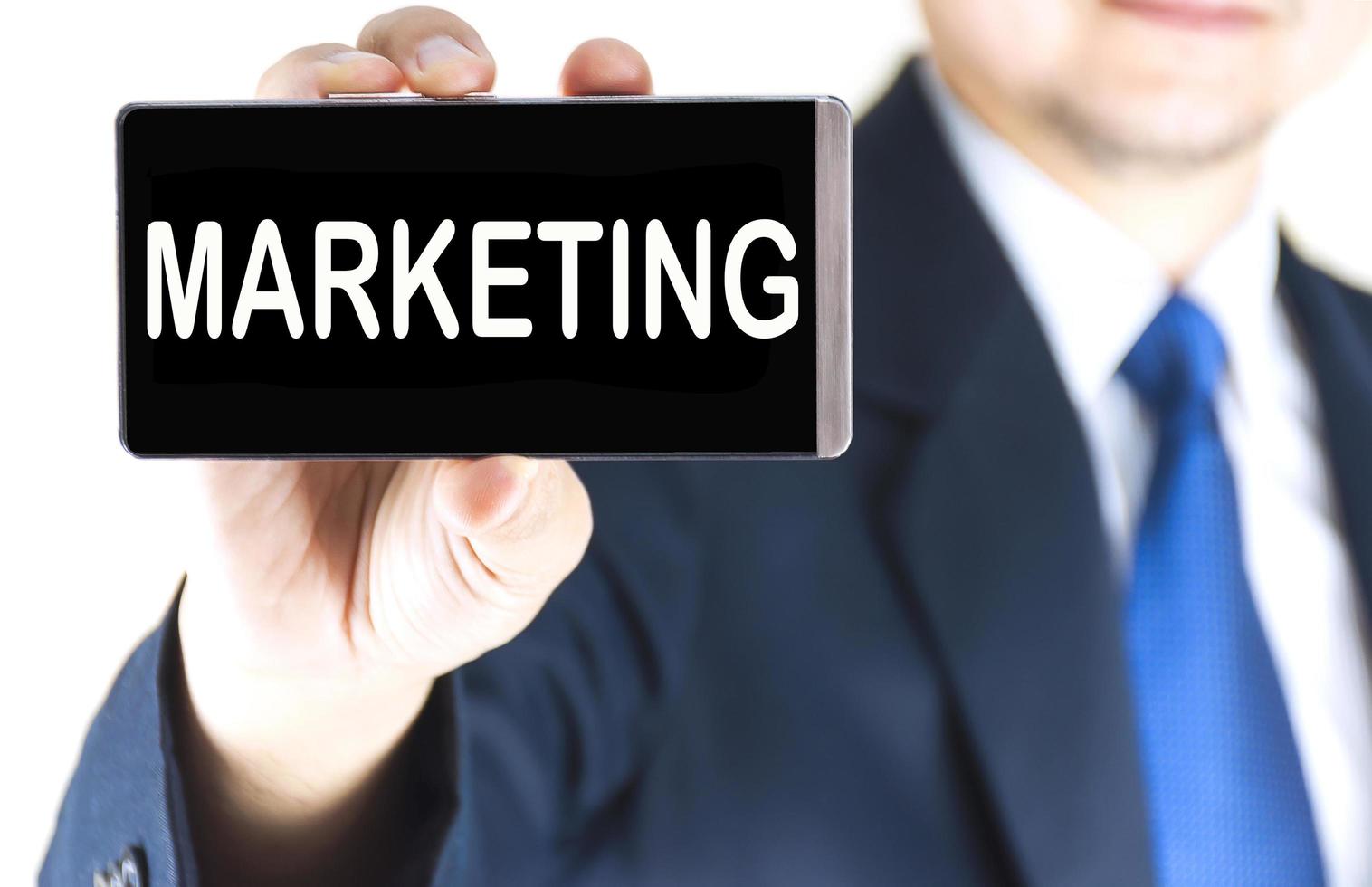 MARKETING word on mobile phone screen in blurred young businessman hand over white background, business concept photo