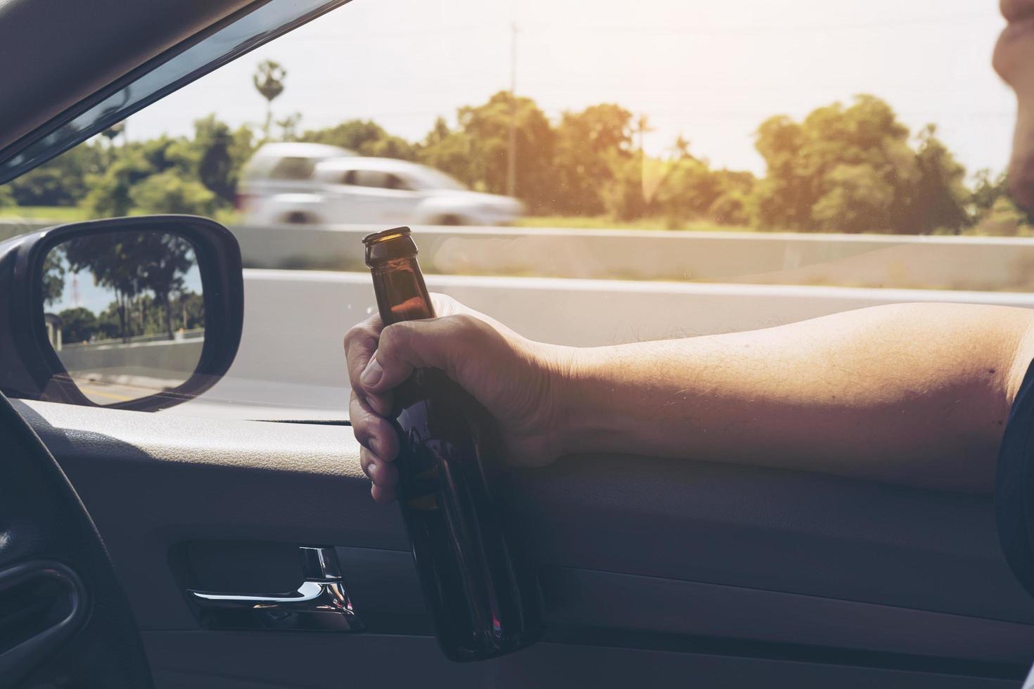 Man holding beer bottle while driving a car photo