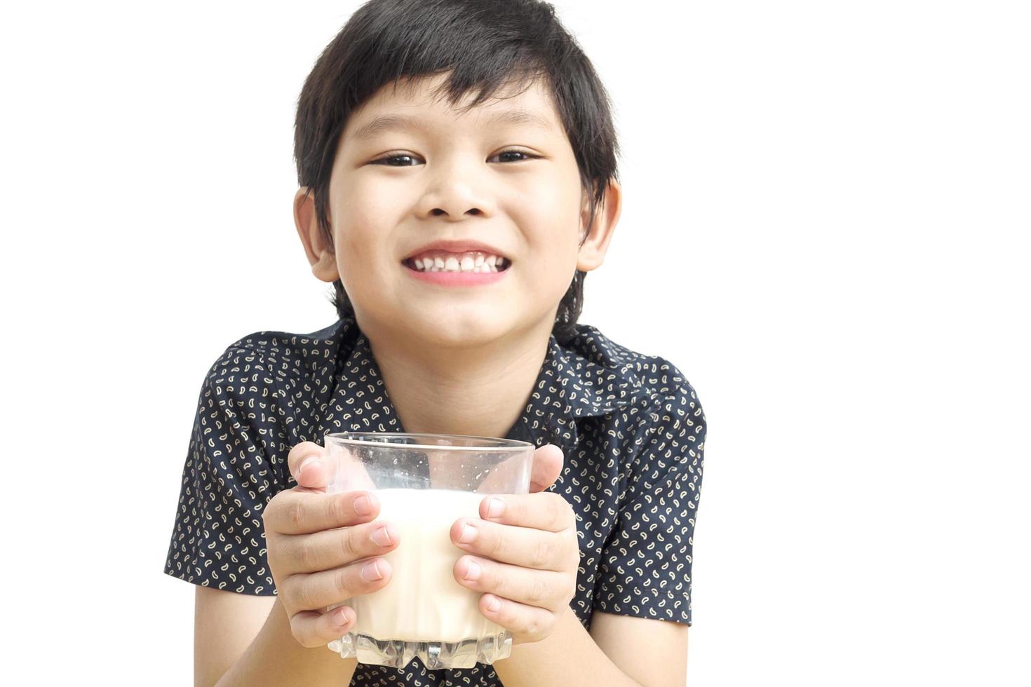 Asian boy is drinking a glass of milk over white background. Photo is focused at his hand.