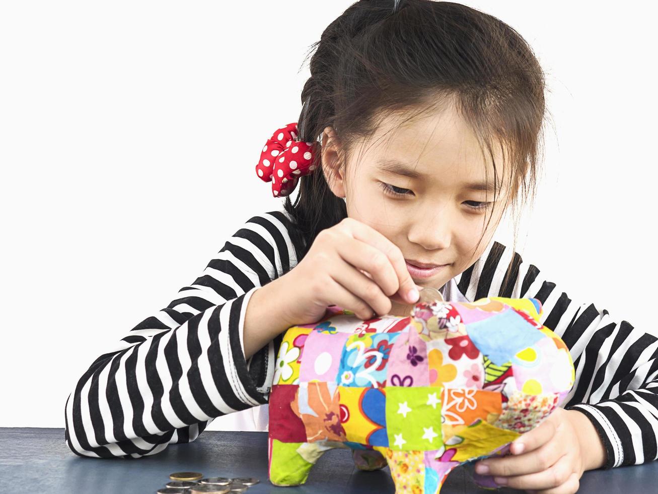 Asian kid is putting money in to a colorful piggy coin bank with calculator on wooden table photo