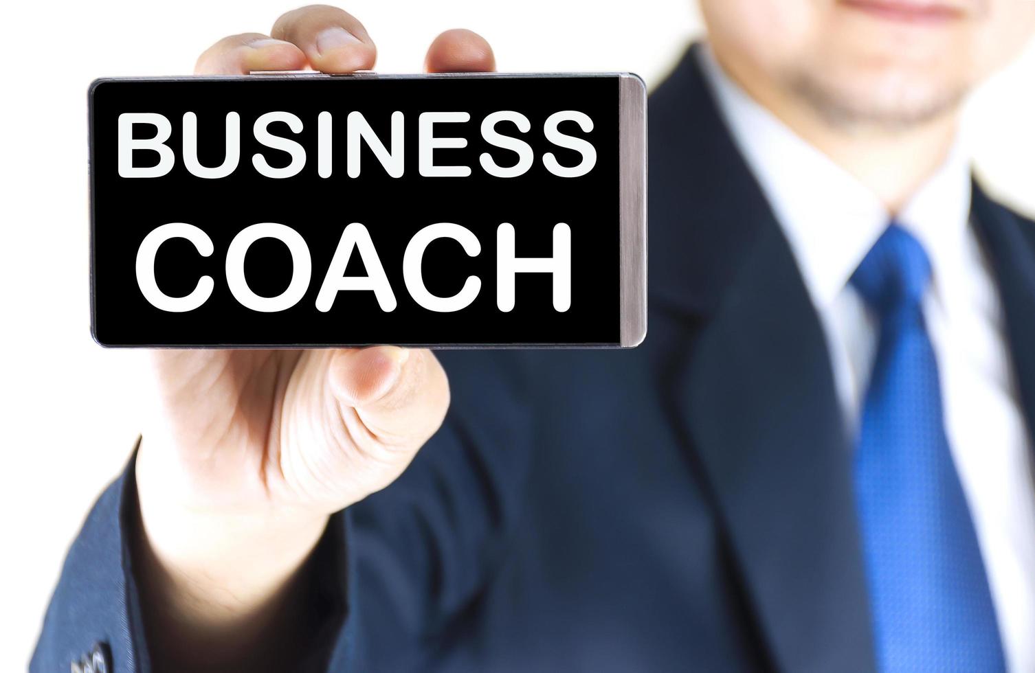 BUSINESS COACH, word on mobile phone screen in blurred young businessman hand over white background, business concept photo