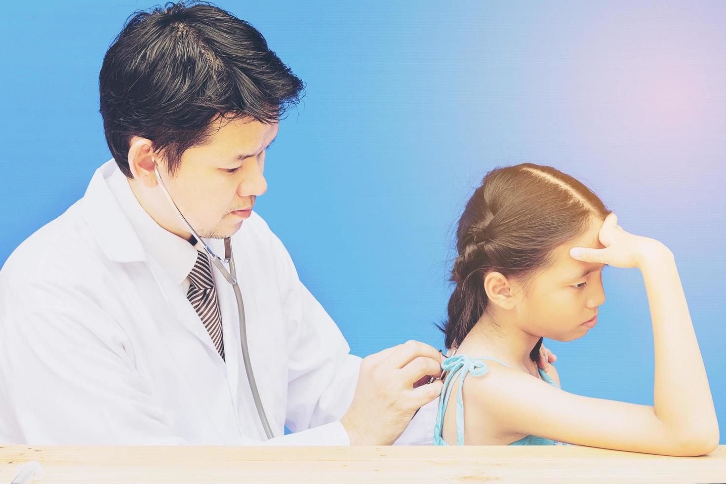 una chica asiática enferma está siendo tratada por un médico de fondo azul foto
