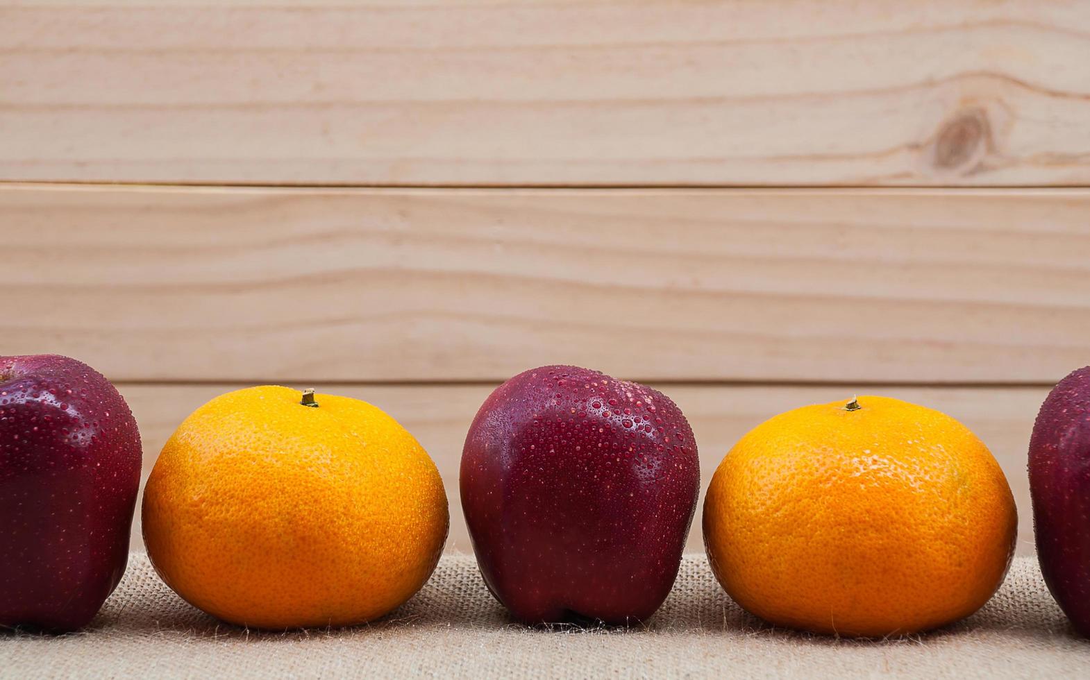 Fresh apples and oranges with water drop putting on sack fabric over wooden background photo