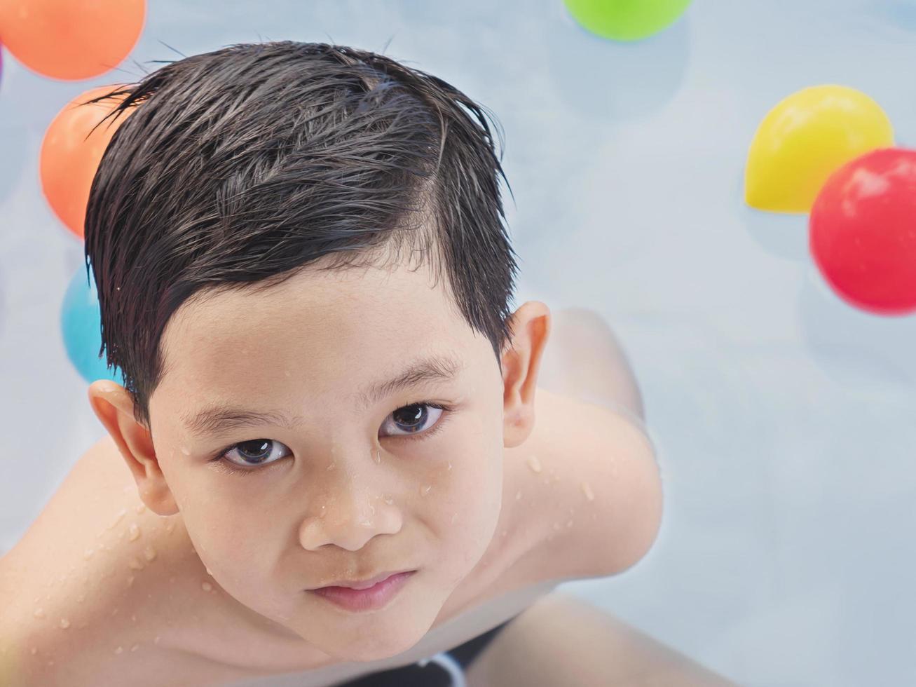 Asian kid is playing in a kid water pool with colorful balls photo