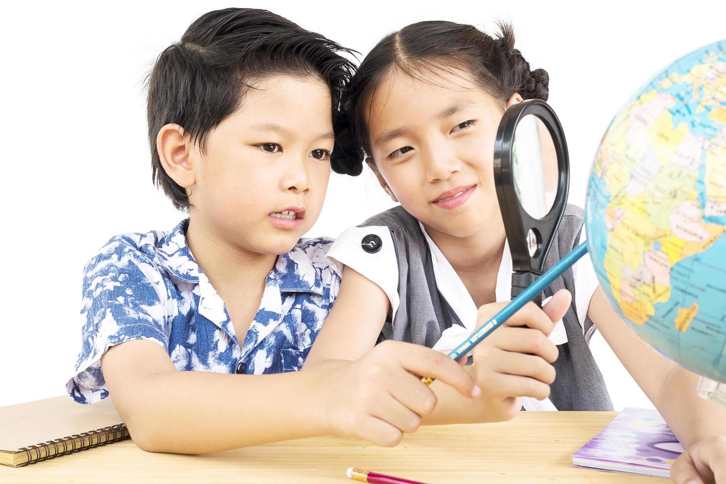 Asian kids are studying the globe using magnifier over white background photo