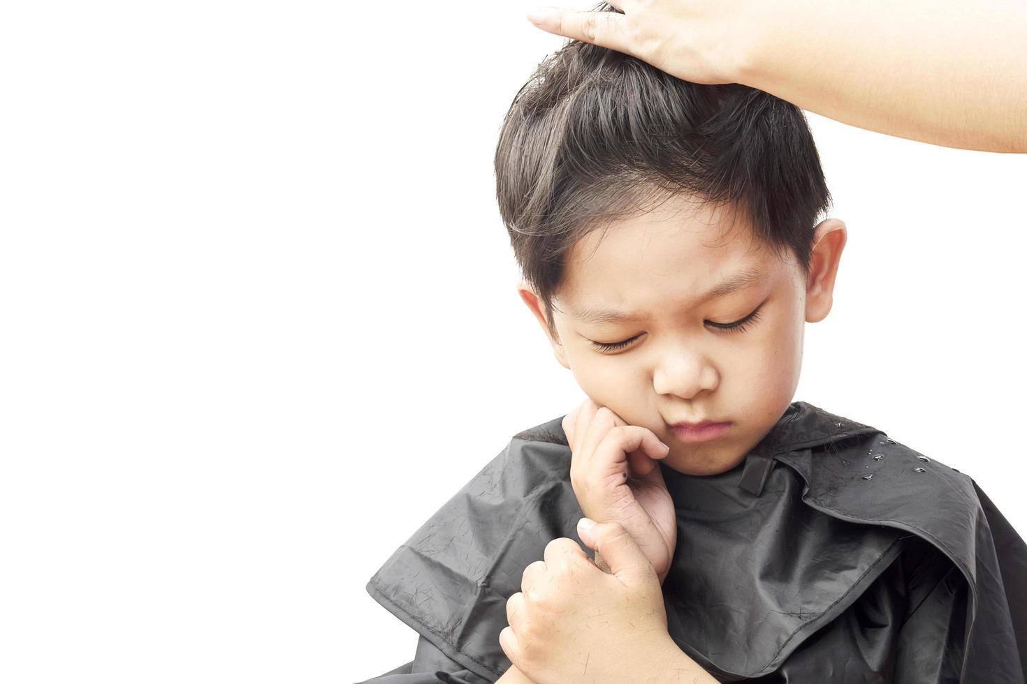 un niño siente picazón mientras se corta el pelo con un peluquero aislado sobre fondo blanco foto