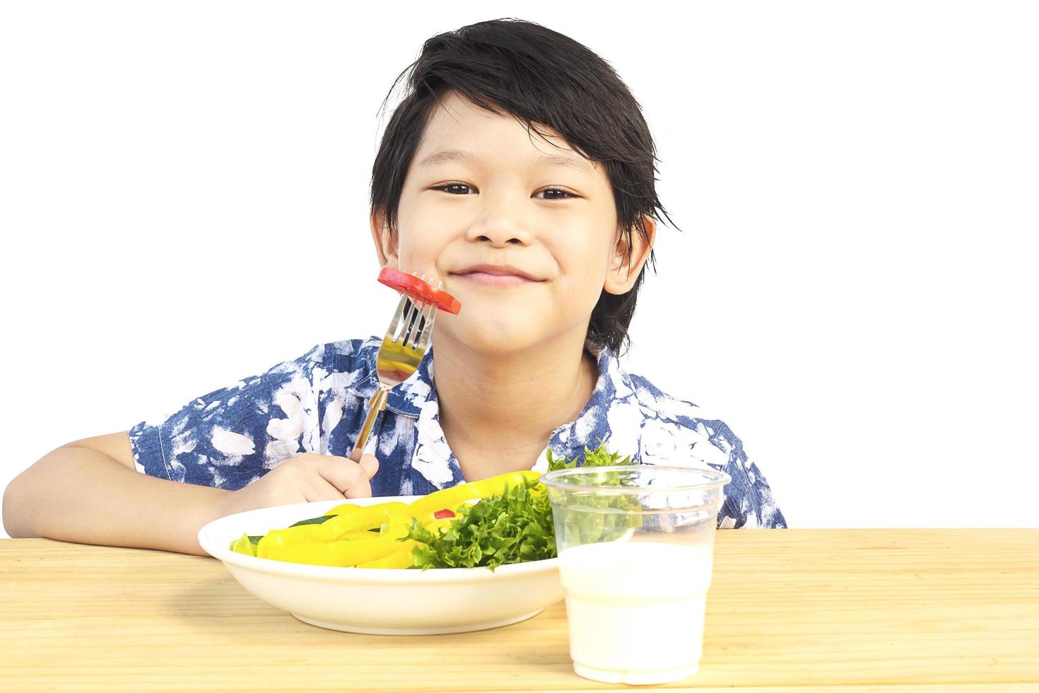 Asian lovely boy showing enjoy expression with fresh colorful vegetables and glass of milk isolated over white background photo