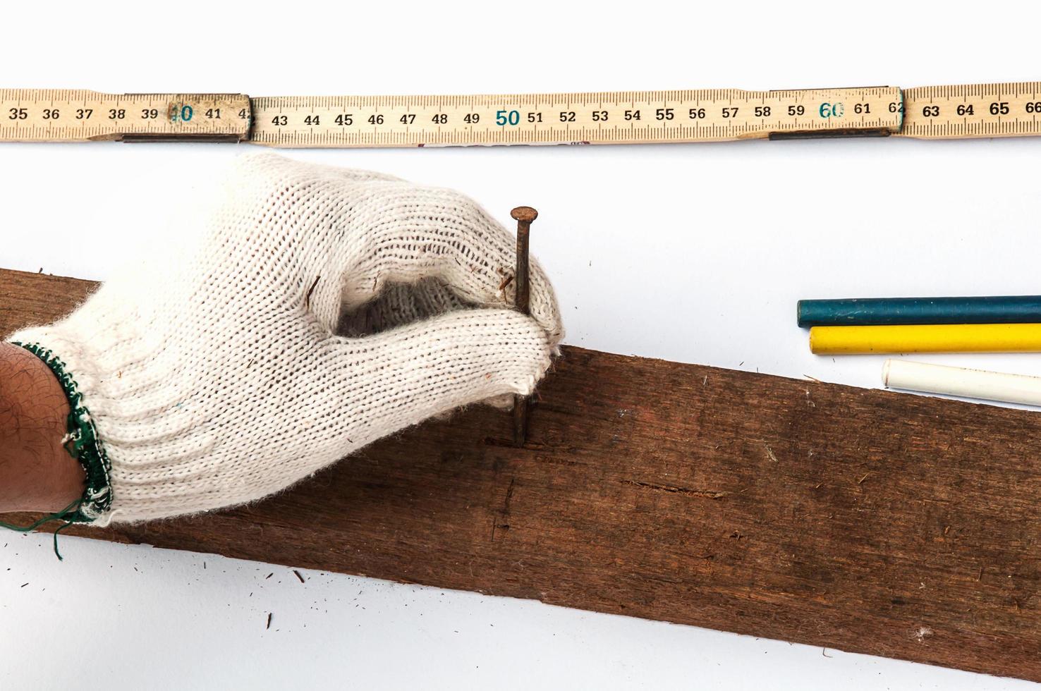 Hand holding nail ready to put it in wooden bar over other tools on white background photo