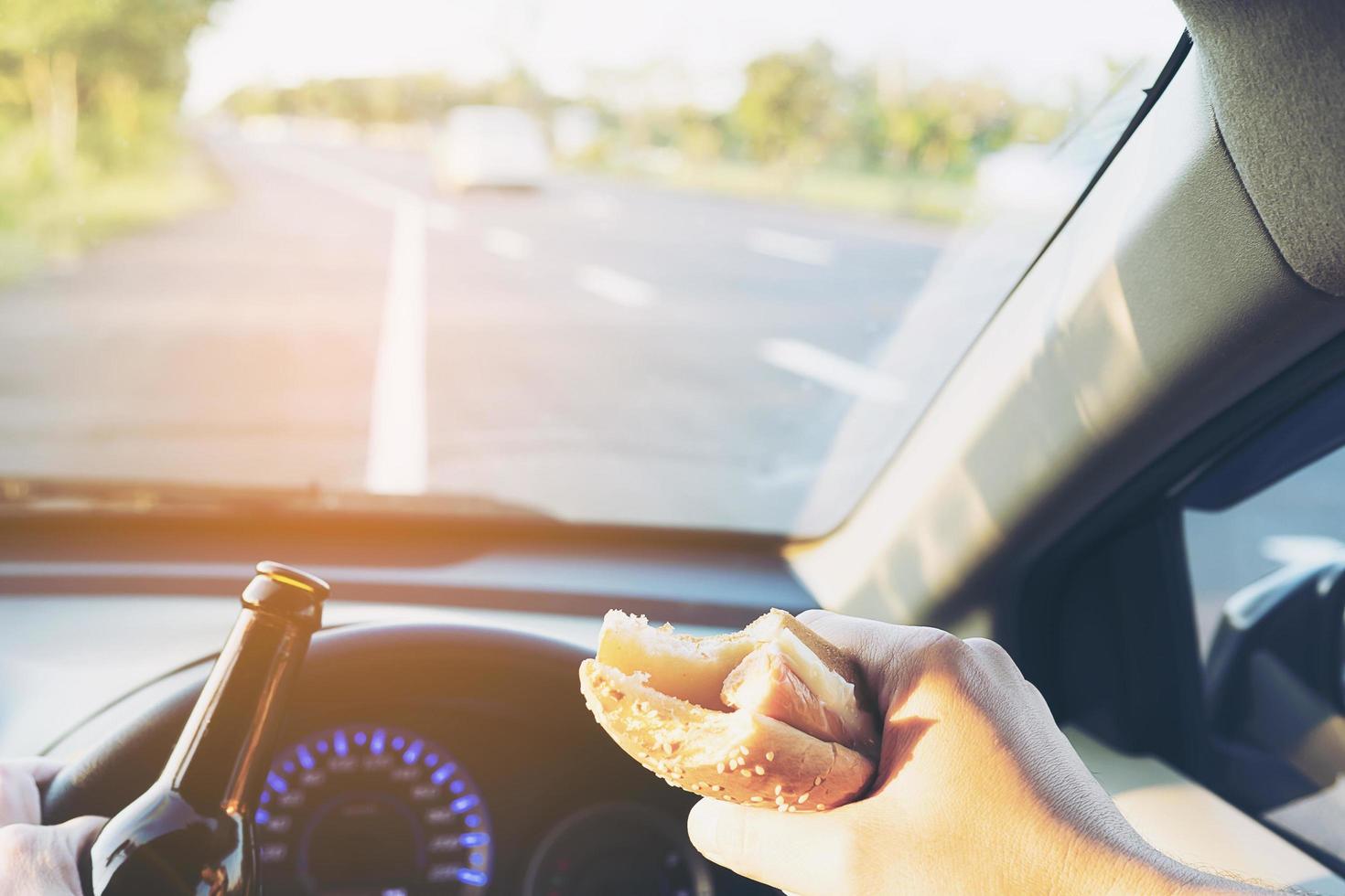 Man eating hotdog with beer while driving a car dangerously photo