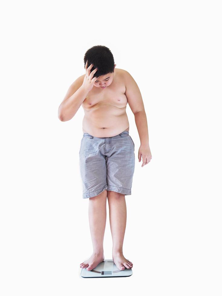 Soft focus of fat boy disappoint his fatness while standing on on weighing machine over white background photo