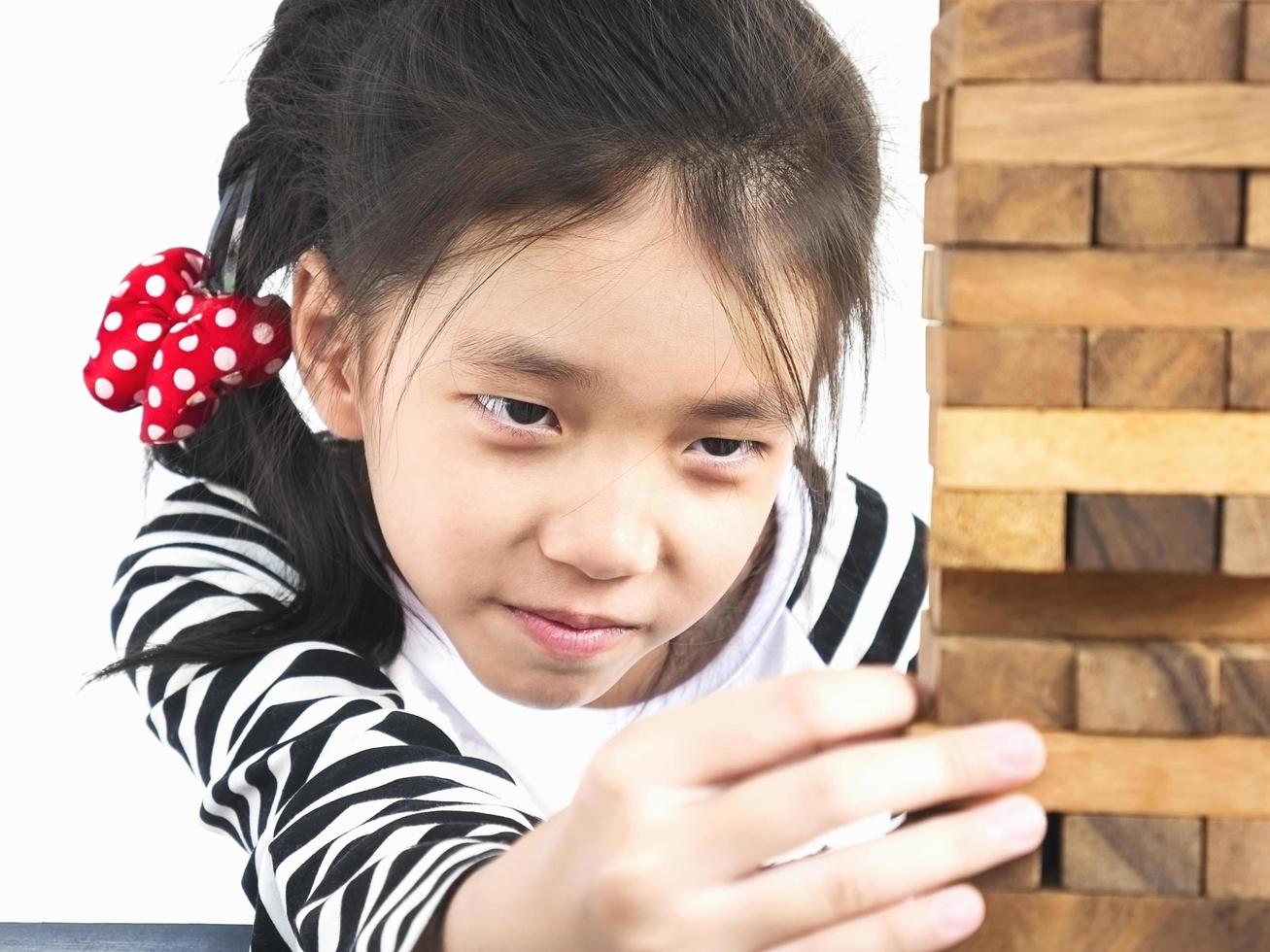 Asian kid is playing wood blocks tower game for practicing physical and mental skill. Photo is focused at model face and isolated over white.