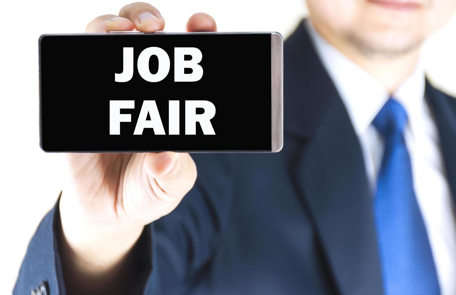 JOB FAIR word on mobile phone screen in blurred young businessman hand over white background, business concept photo