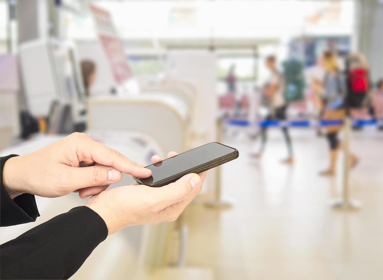 Businessman is using - touching mobile phone over blurred travelers and check-in counter in airport terminal photo