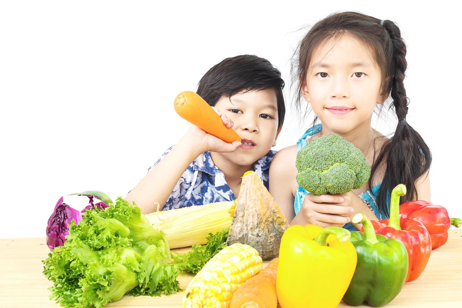 Asian boy and girl showing enjoy expression with fresh colorful vegetables isolated over white background photo