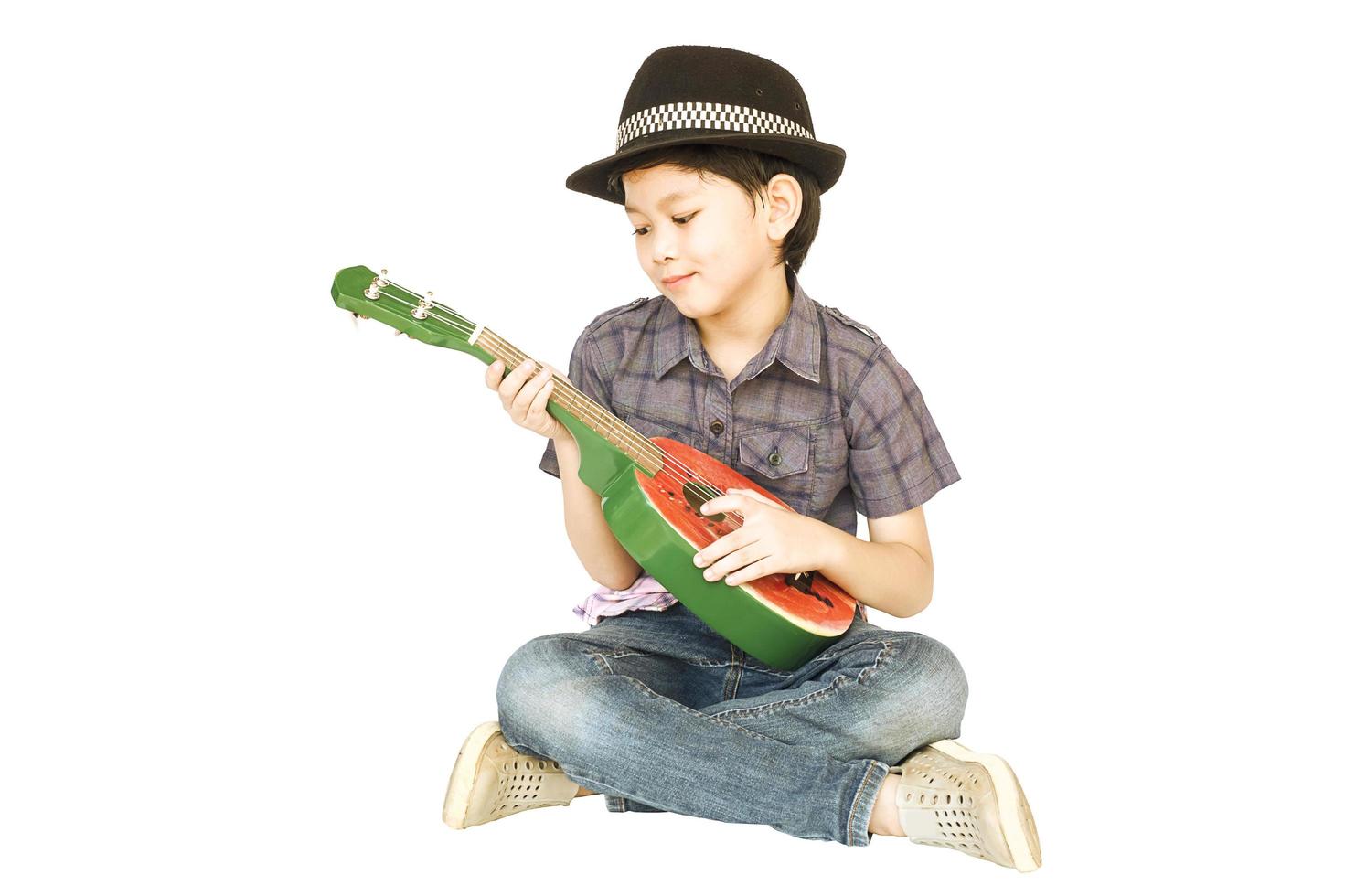 7 years old Asian boy is sitting and playing ukulele isolated over white. photo