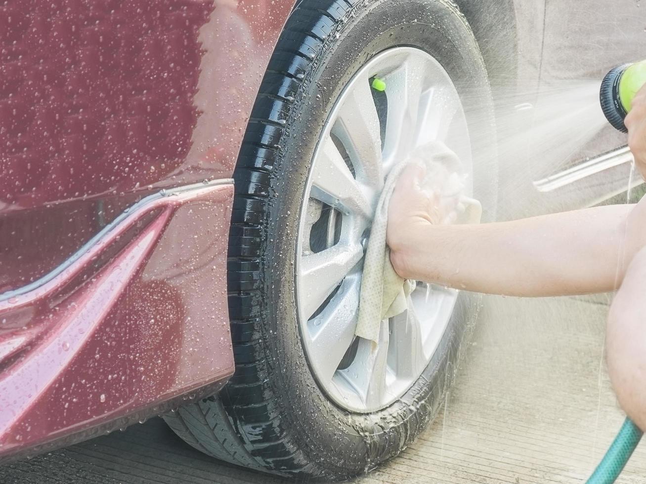 A man's hand is cleaning a car wheel using cloth and spray water photo