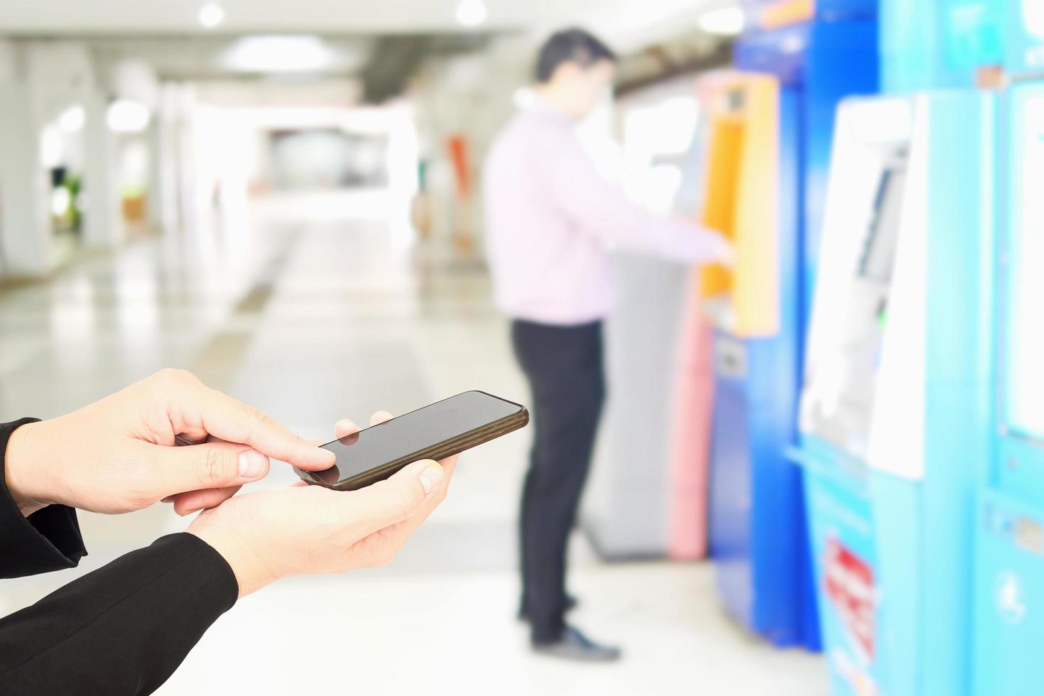 Businessman is using mobile phone over blurred background of man using ATM photo