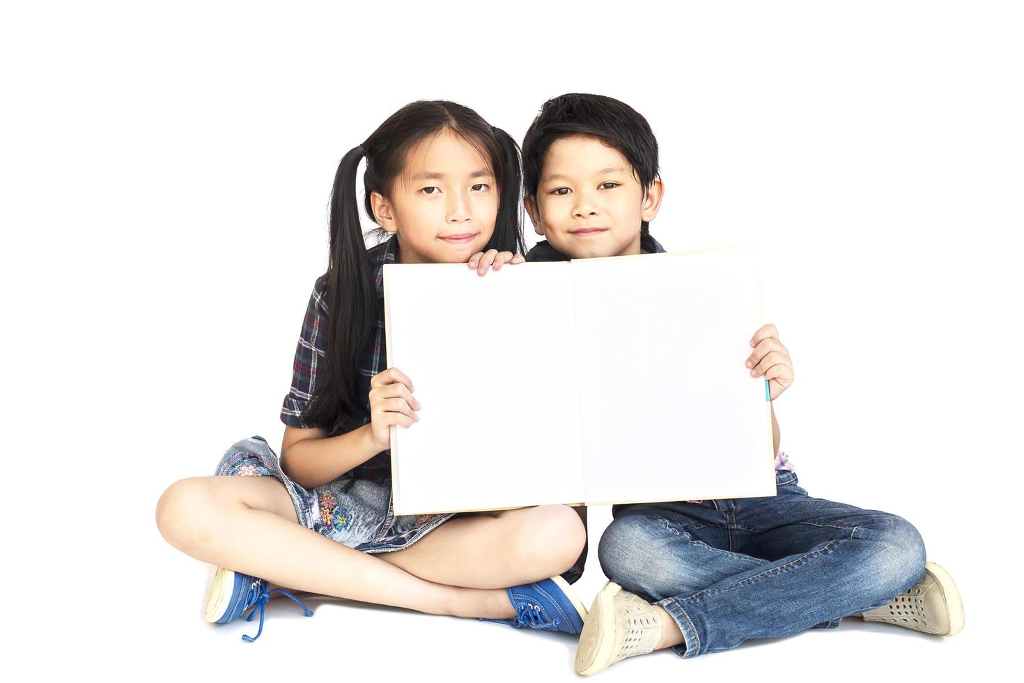 Niña y niño de la escuela asiática de 10 y 7 años mostrando felizmente un libro blanco vacío aislado en blanco foto