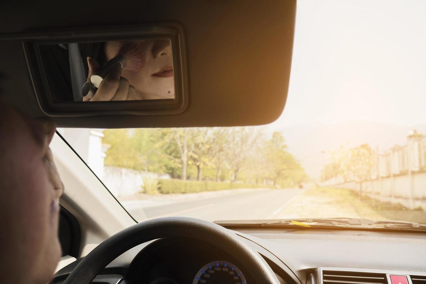 Woman makeup her face using blush brush while driving car, unsafe behavior photo