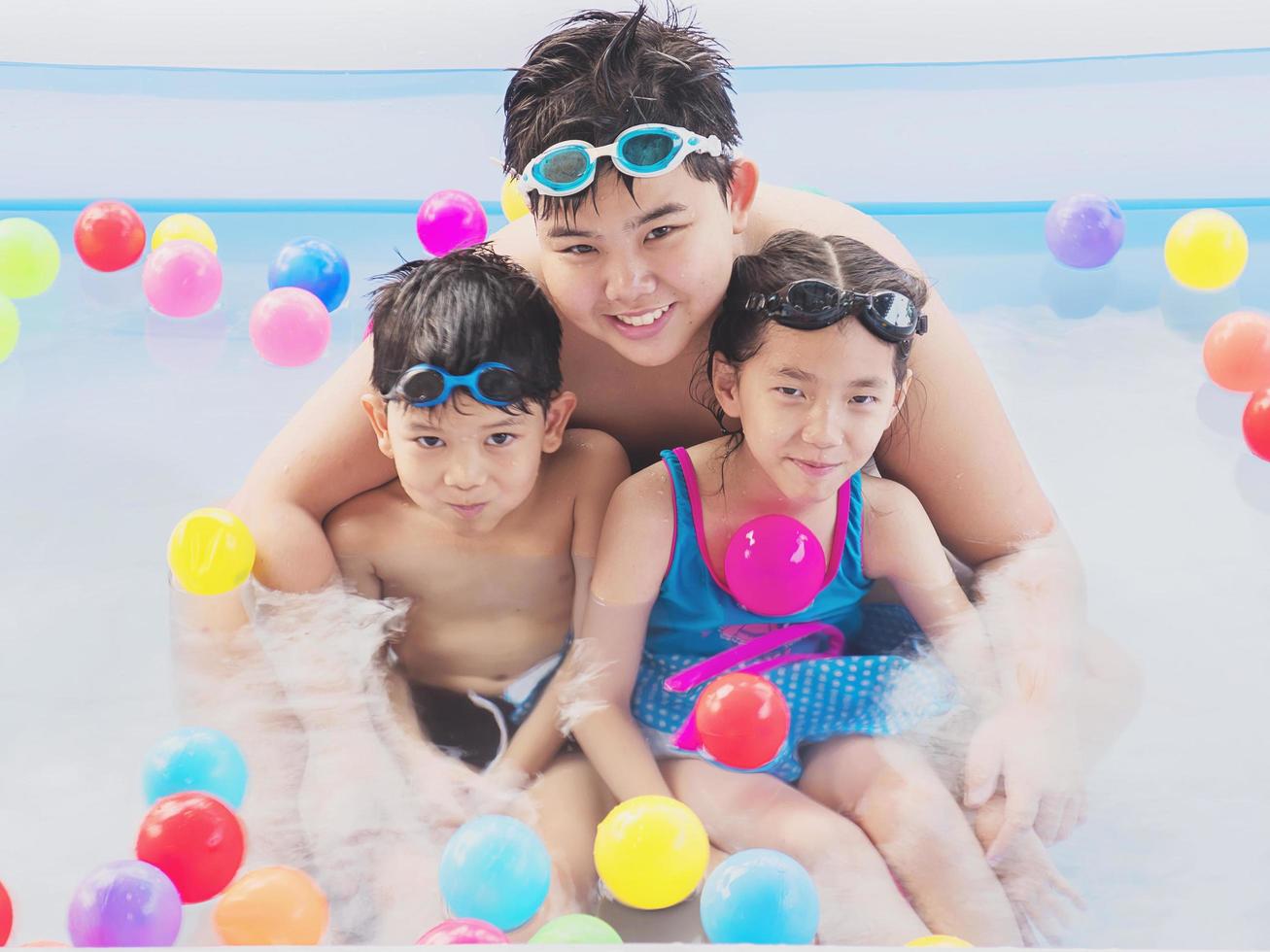 Asian brotherhood are playing in a kid water pool with colorful balls. Photo is focused at the biggest kid's face.