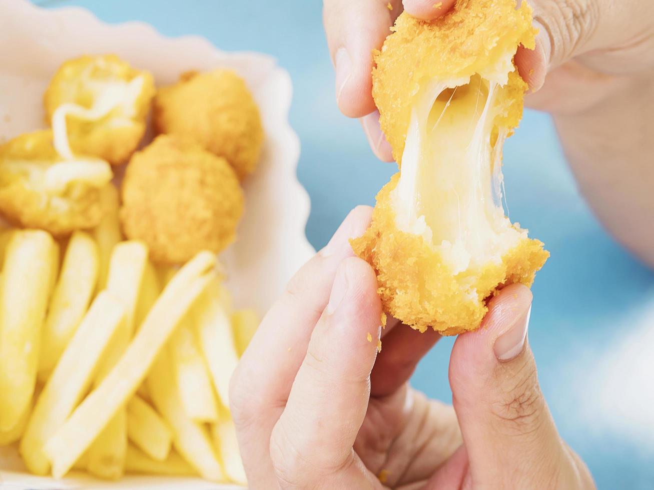 la mano está sosteniendo una bola de queso estirada lista para ser comida con papas fritas suaves enfocadas en el fondo de la mesa azul foto