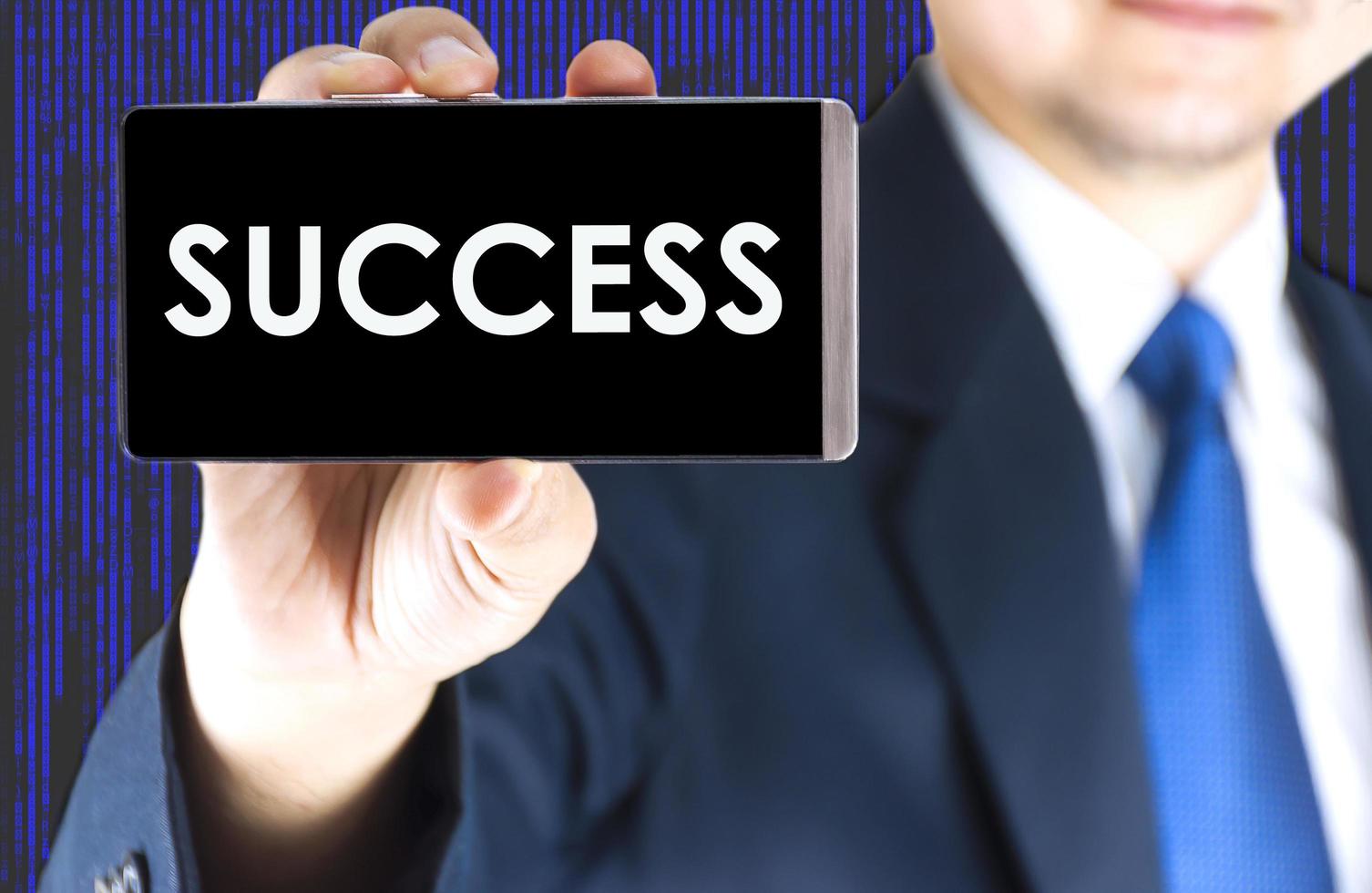 SUCCESS word on mobile phone screen in blurred young businessman hand and digital technology background, business concept photo