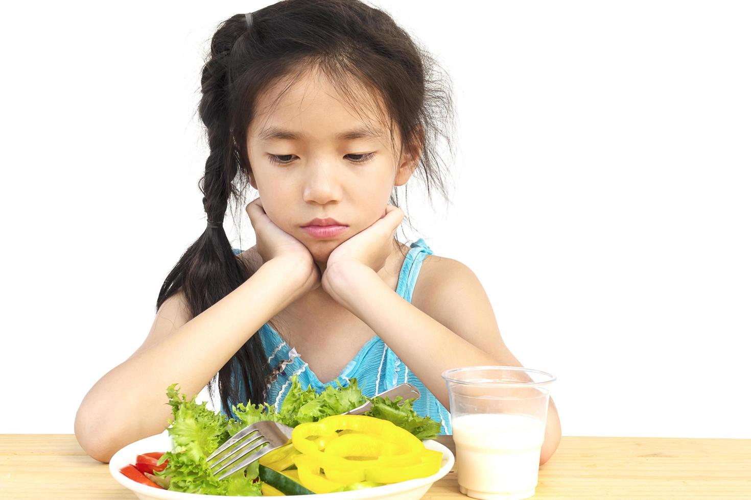 Asian lovely girl showing boring expression with fresh colorful vegetables and glass of milk isolated over white background photo