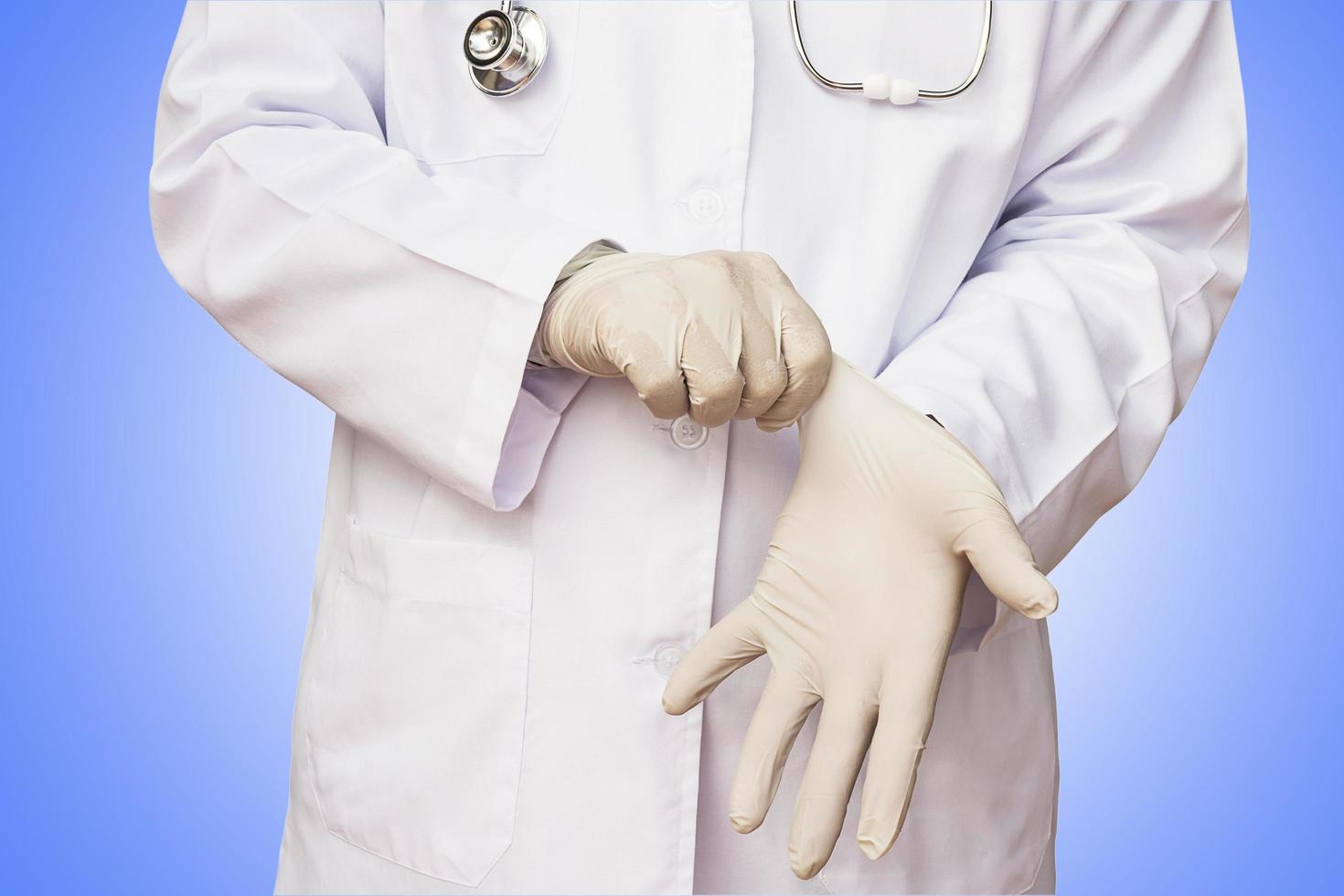 el médico varón está poniendo guantes listos para examinar a su paciente con un fondo azul degradado claro. la foto incluye el camino de recortes.